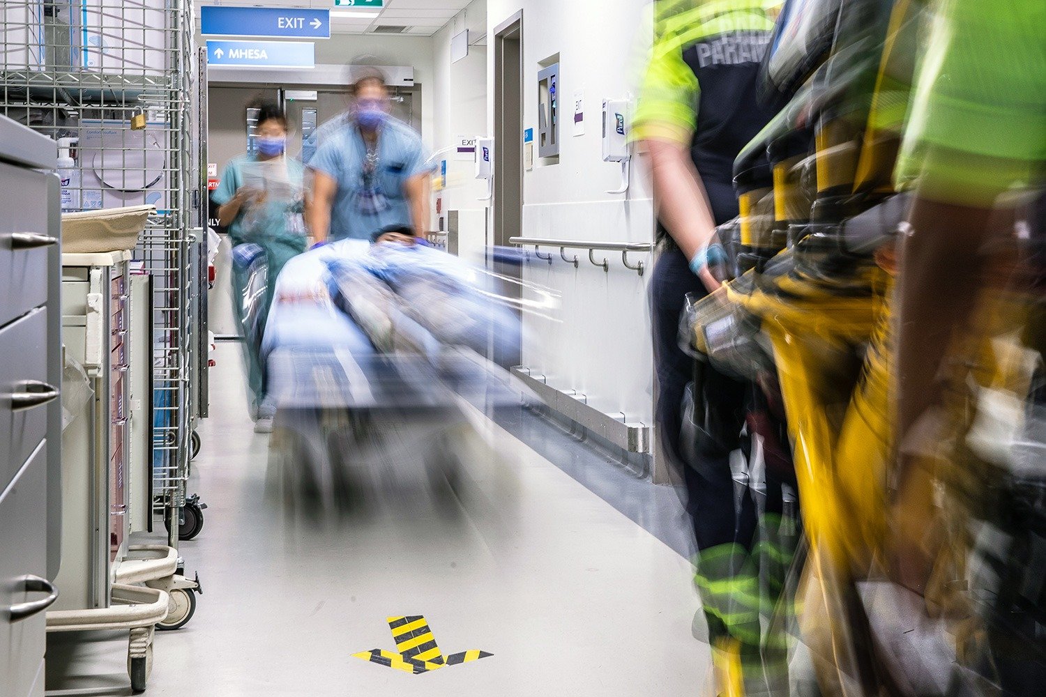 A busy hospital hallway with blurry paramedics rushing by with a hospital bed