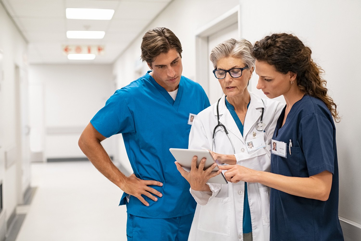 A doctor and two nurses review a tablet in a hospital hallway
